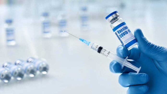 Male doctor hand wears glove holding syringe and vial with covid 19 vaccine.